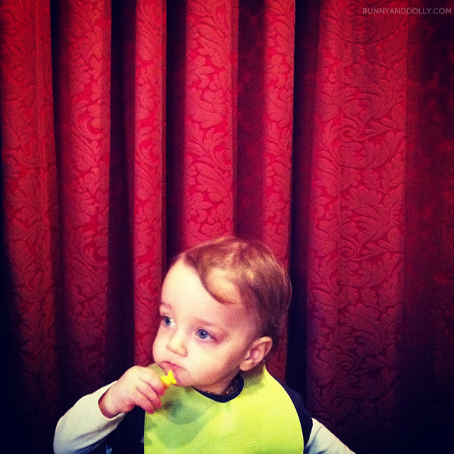 toddler eating goldfish crackers in front of red curtain